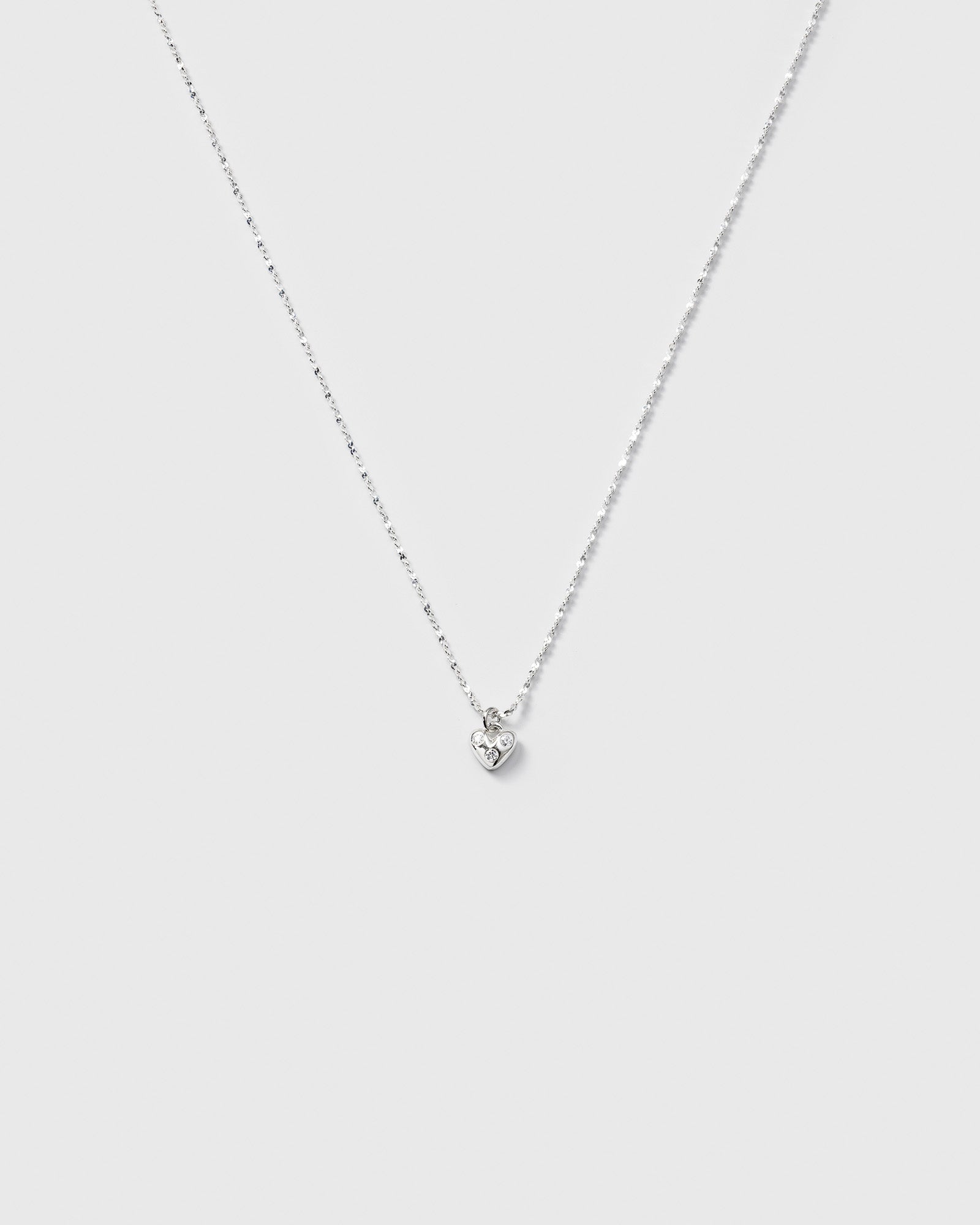 A product shot of the Forever Necklace in silver, showcasing its delicate twisted chain and a small heart pendant set with sparkling cubic zirconia stones.