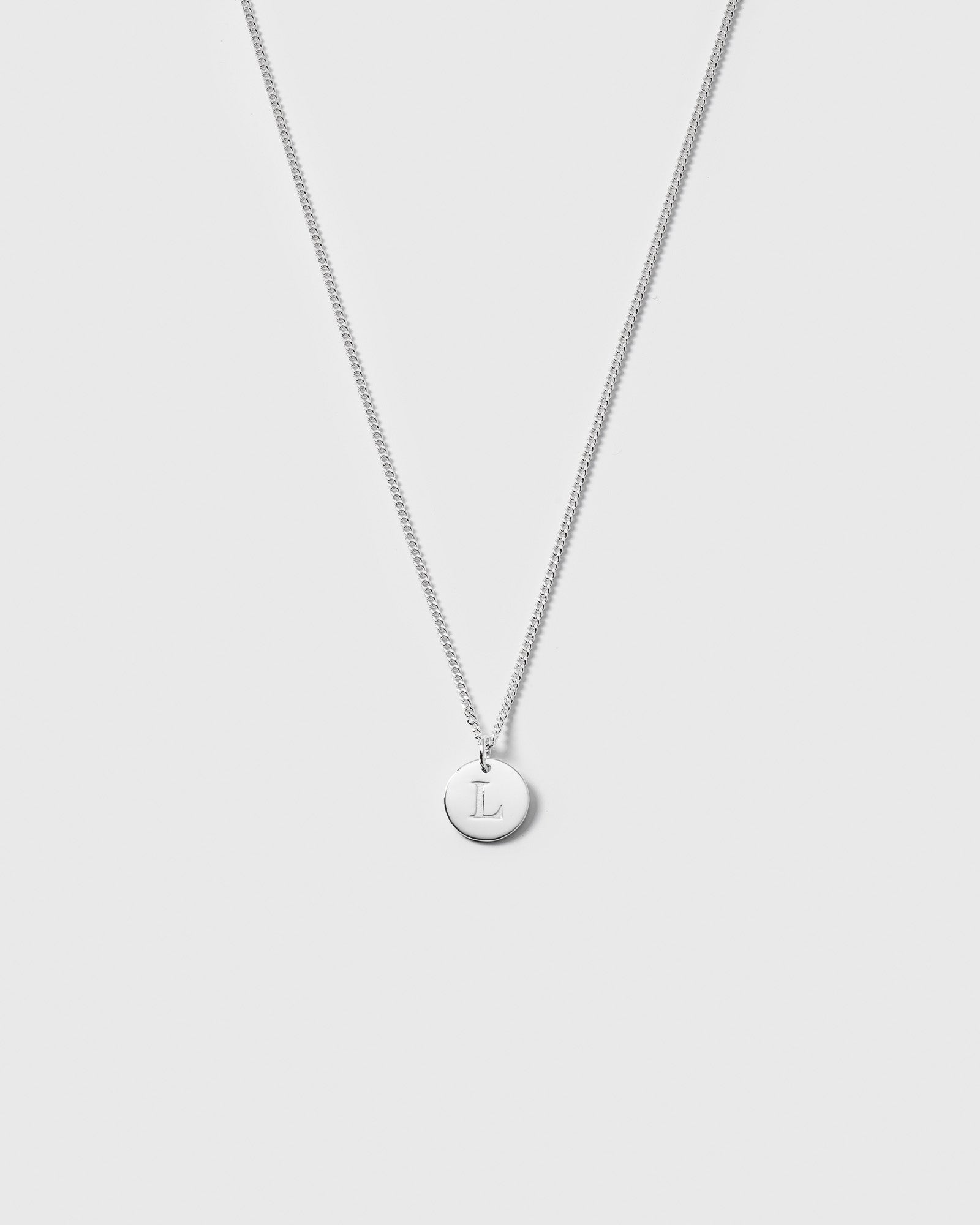 A product shot of the Beloved Short Curb Chain in silver, featuring a round pendant engraved with the letter L.