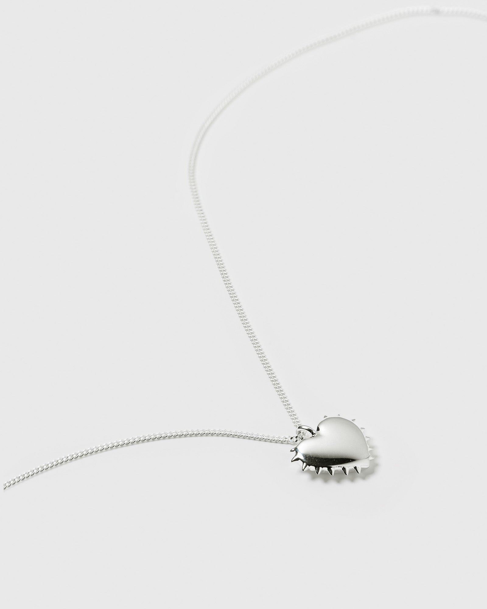 A product shot of the True Love Spike Heart Necklace in silver, laid out to display its fine chain and heart-shaped pendant with a spiky border.