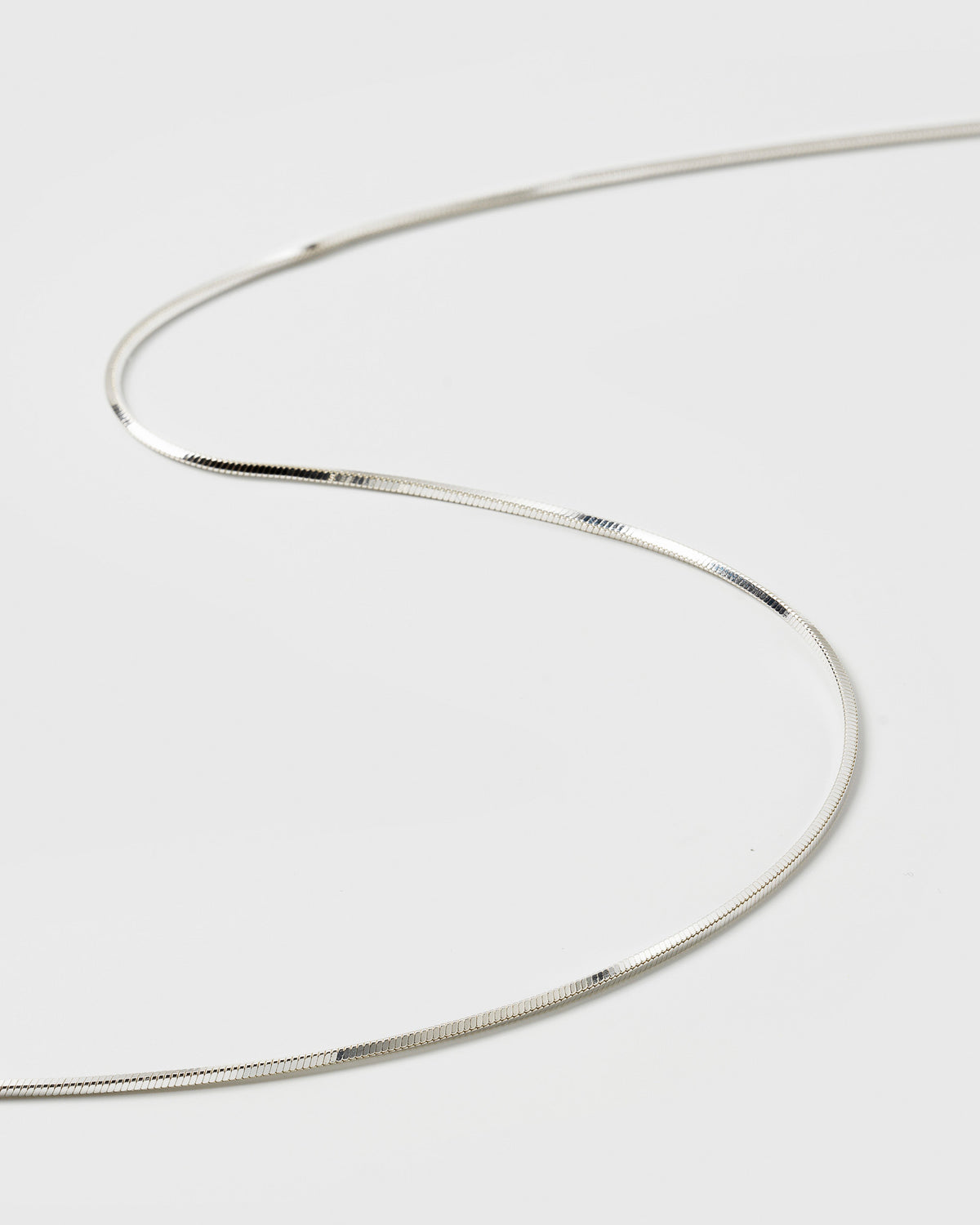 A product shot of the Sheer Mirror Necklace in silver, showing a close-up of its smooth, flat, and reflective snake chain design.