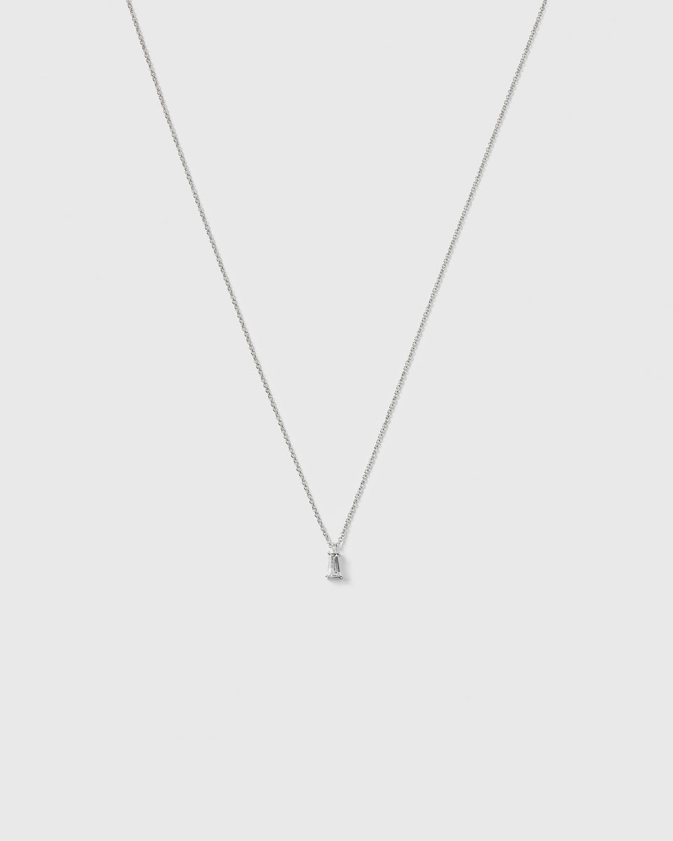 A product shot of the Iggy Necklace in silver, featuring a fine chain and a small pendant with a single, tapered baguette-cut cubic zirconia.