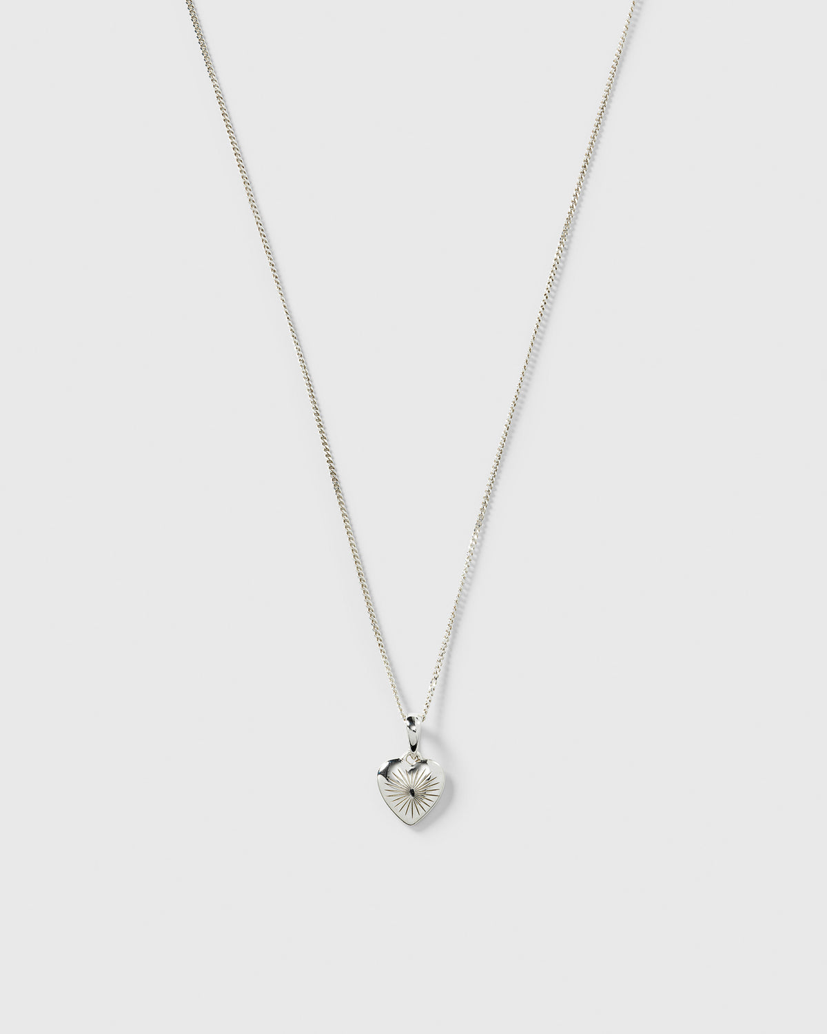 A product shot of the Sunburst Heart Necklace in silver, featuring a fine chain and a heart-shaped pendant with an engraved sunburst pattern.
