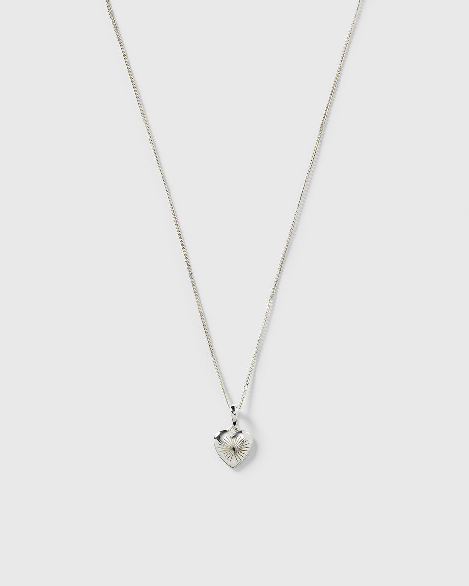 A product shot of the Sunburst Heart Necklace in silver, featuring a fine chain and a heart-shaped pendant with an engraved sunburst pattern.