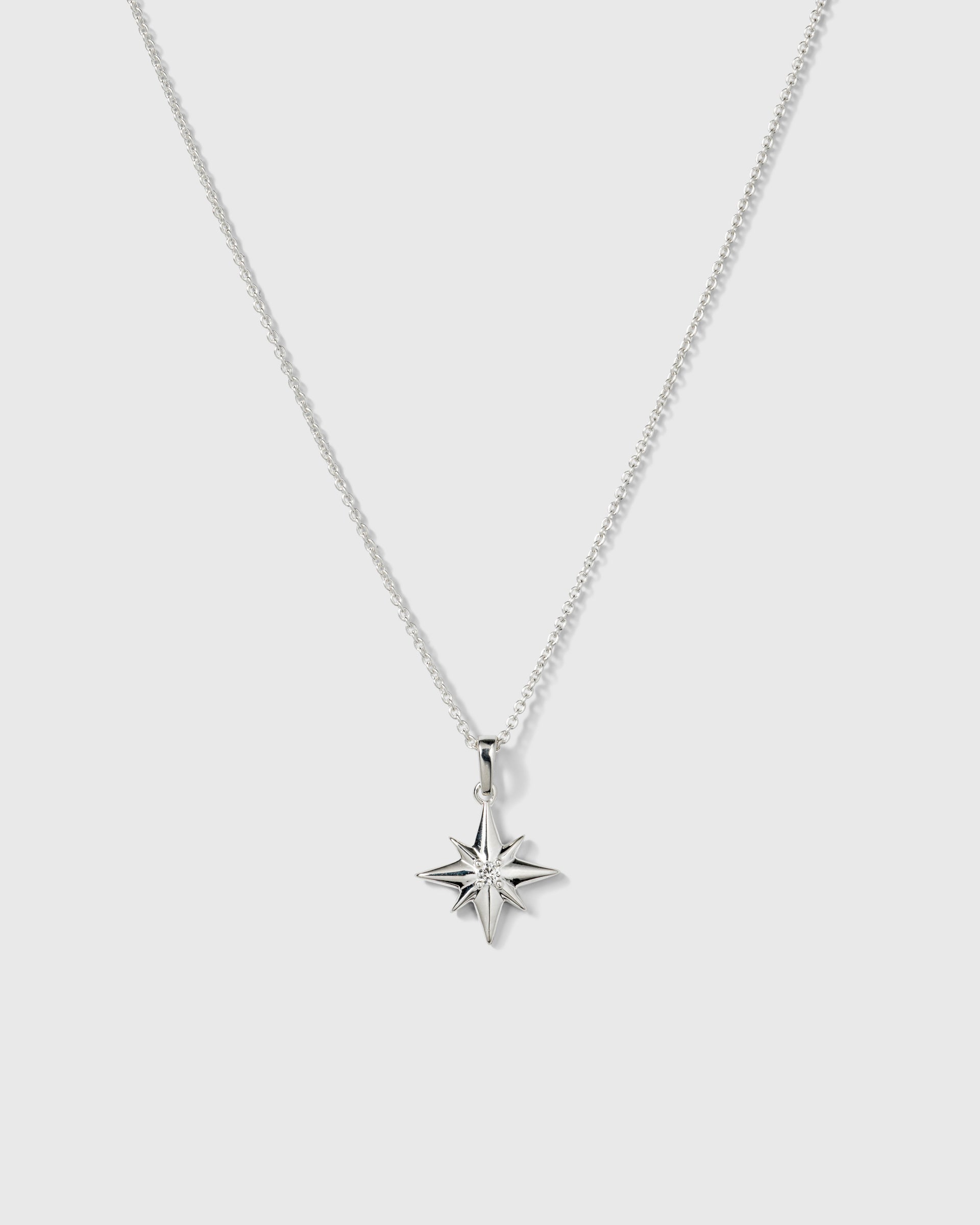 A product shot of the North Star Big Necklace in silver, featuring a delicate chain and a pendant shaped like an eight-pointed star with a crystal at its center.