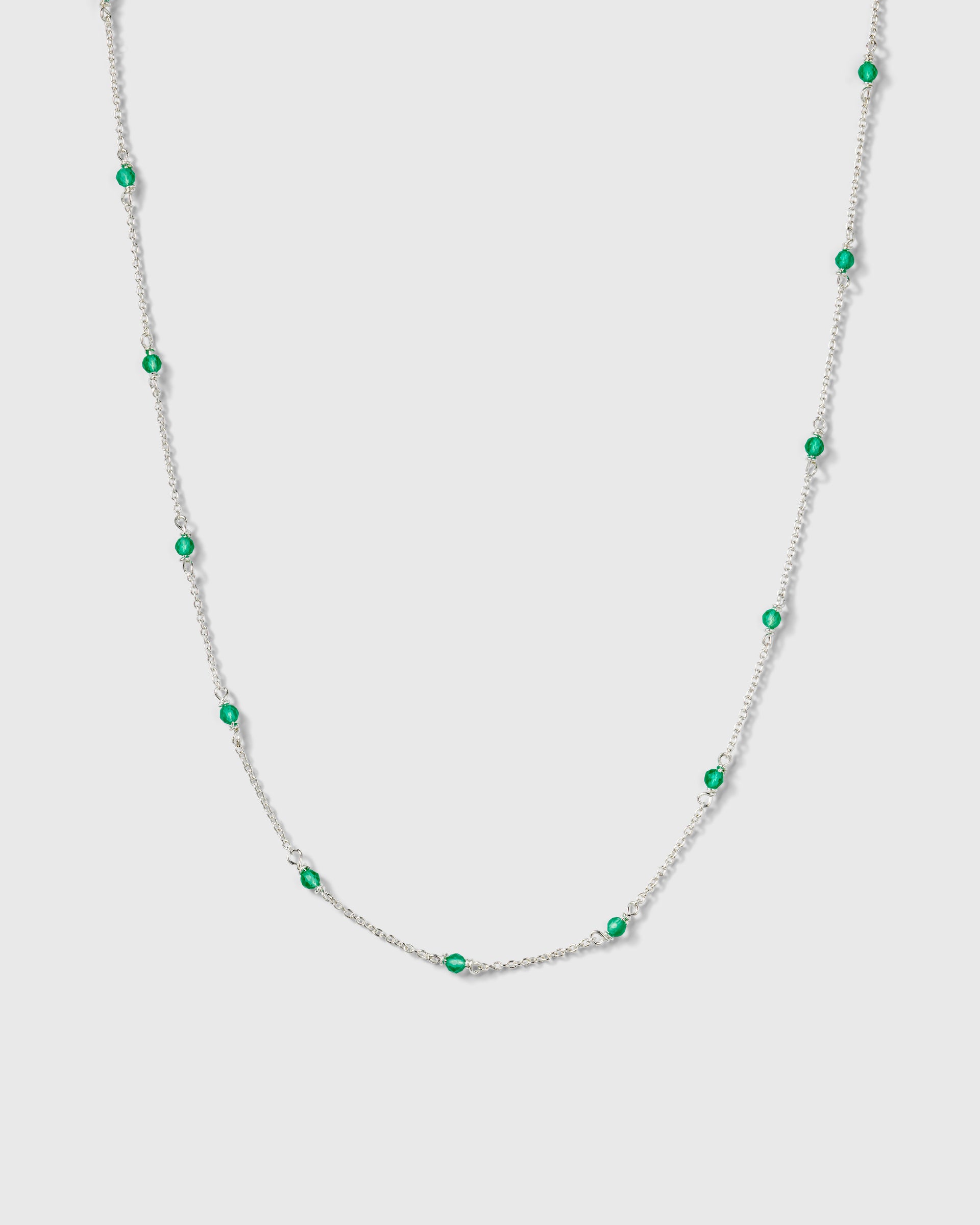 A product shot of the Santa Monica Necklace in silver, featuring a delicate chain with small, vibrant green onyx stones spaced throughout.