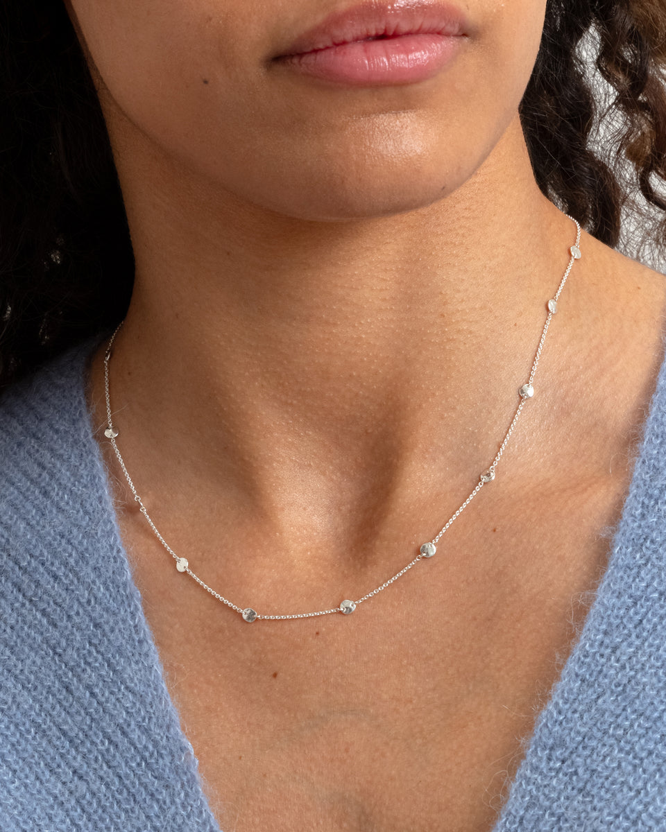 A close-up on a model's neck as she wears the Solea Necklace in silver, showing its delicate chain decorated with small, round hammered circles spaced along it.