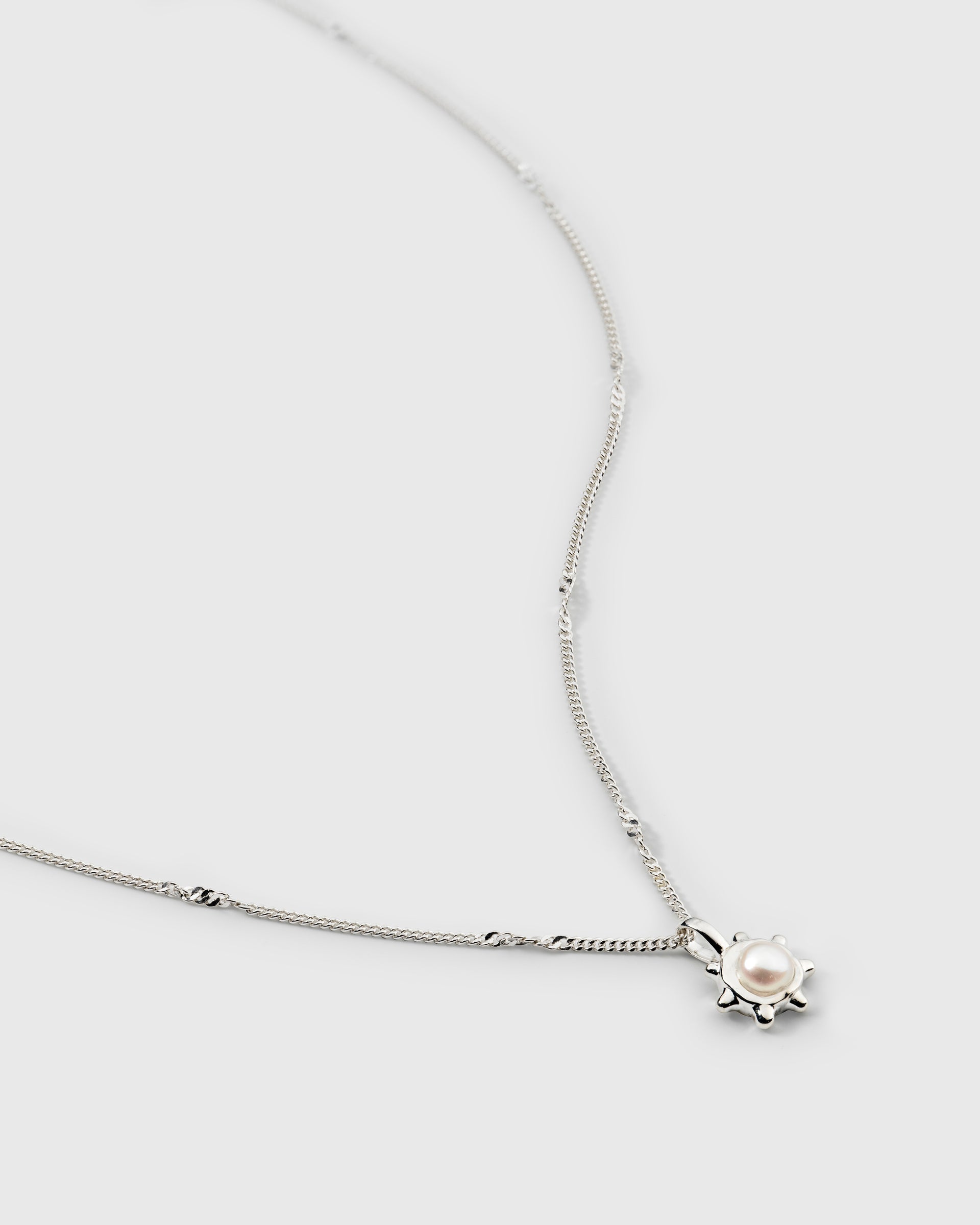 A silver necklace with a sun-shaped pendant featuring a central freshwater pearl on a delicate chain.