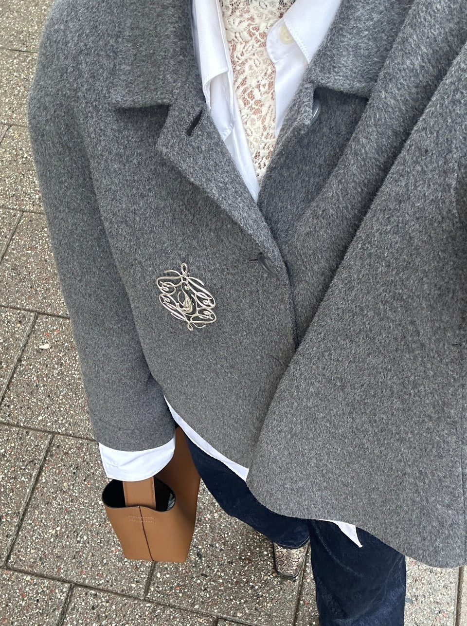 A lifestyle photo of the Ophelia Brooch in silver pinned to the lapel of a grey blazer, worn over a white shirt and lace top.