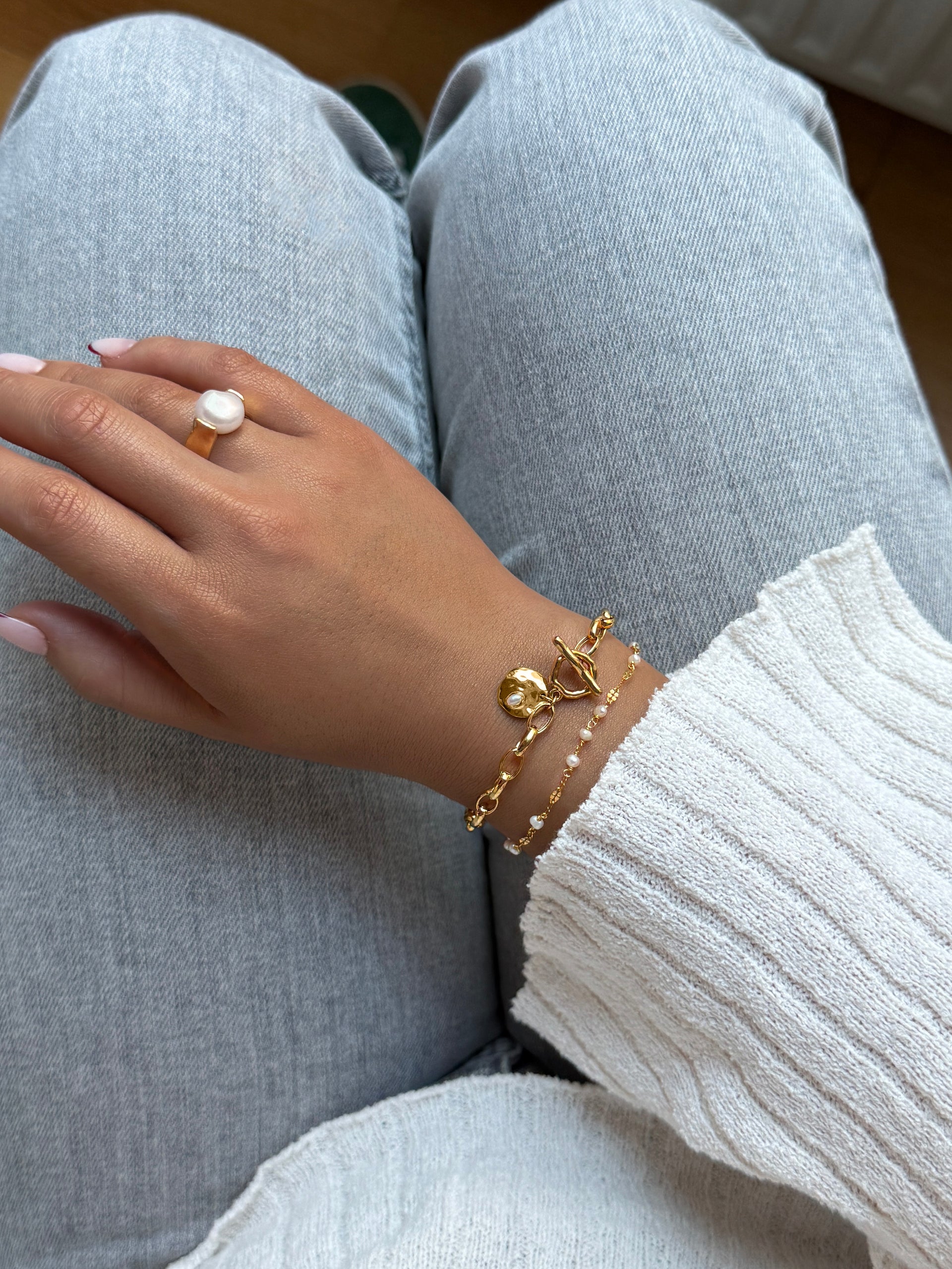 A thicker gold necklace with a small freshwater pearl together with a smaller bracelet with small gold details and small multiple pearls on it. then a larger ring with a large freshwater pearl. 