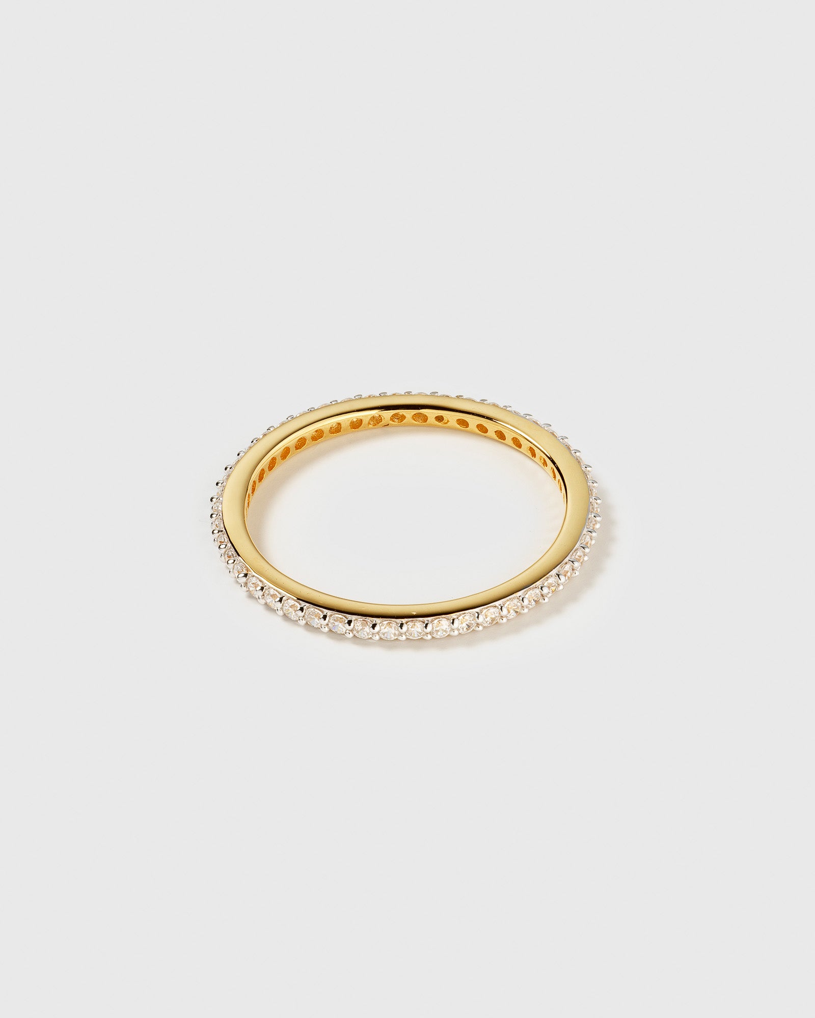 A product shot of the Tiny Sparkle Ring in gold, an eternity band fully set with small, sparkling white zirconias.