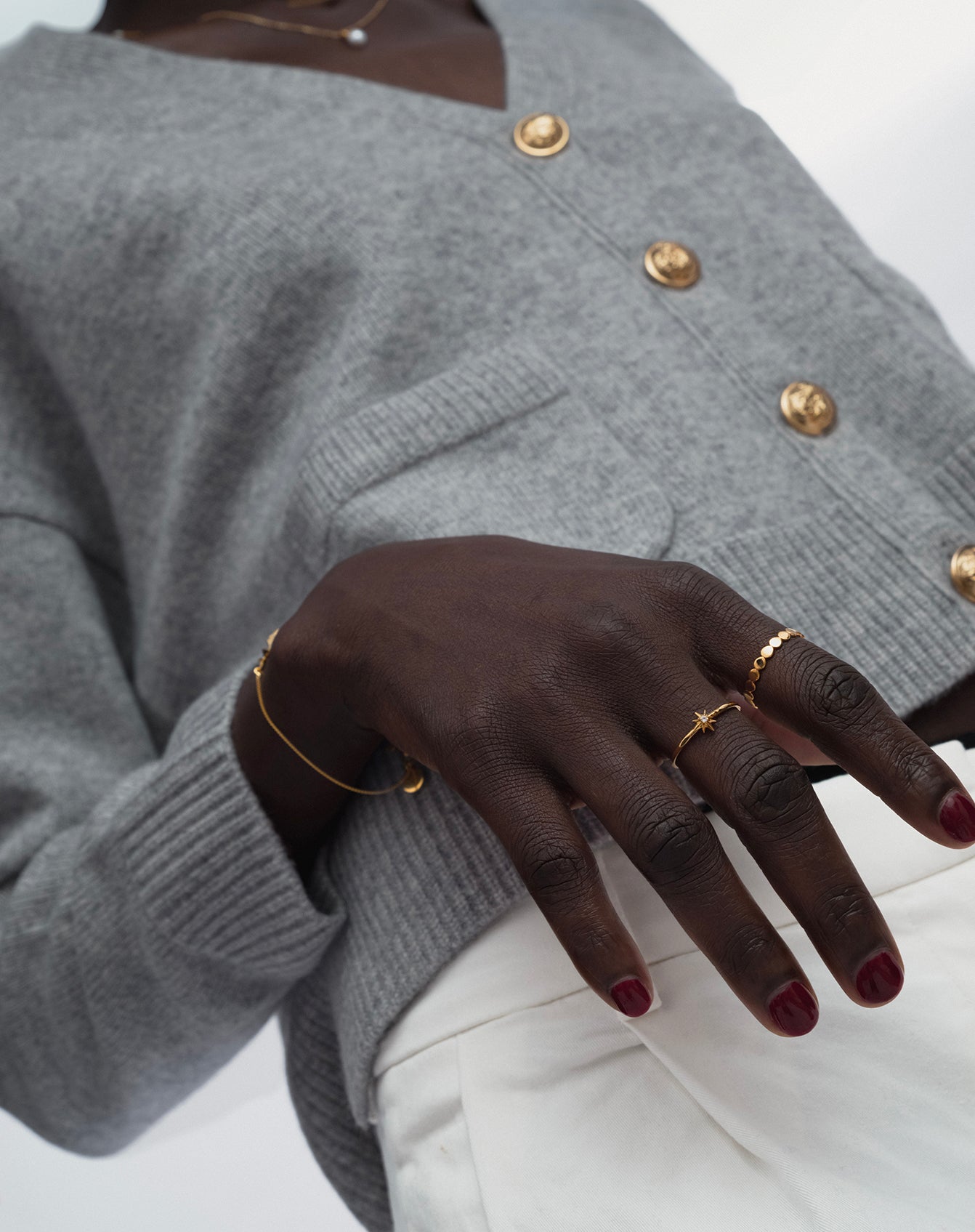A model wearing the Beaches Flat Dots Ring Gold on her index finger, alongside a delicate star-shaped ring on her ring finger, a fine gold bracelet, and a gold necklace with a pearl.