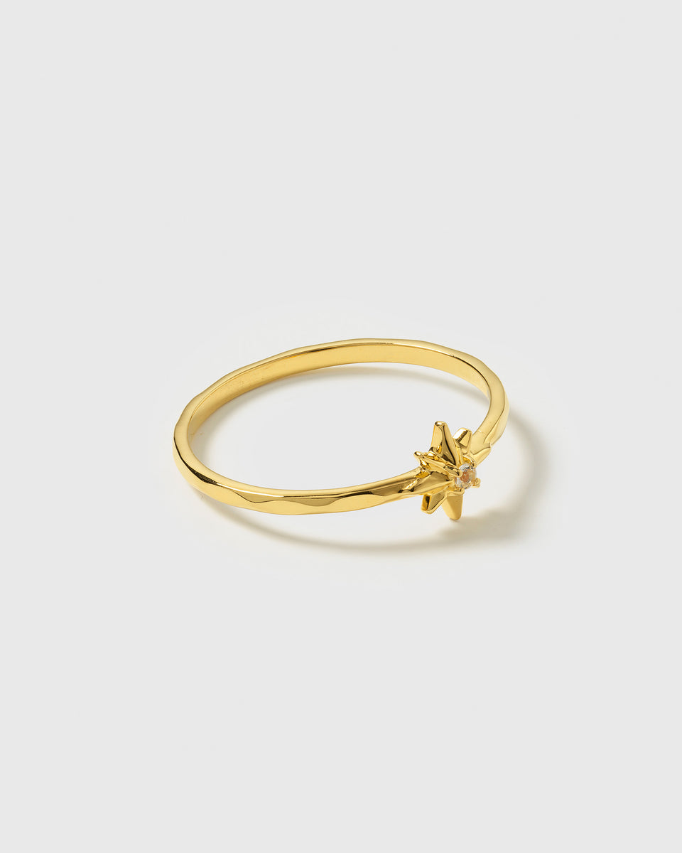 A product shot of the North Star Ring in gold, a thin and neat ring decorated with a star motif and a faceted crystal.