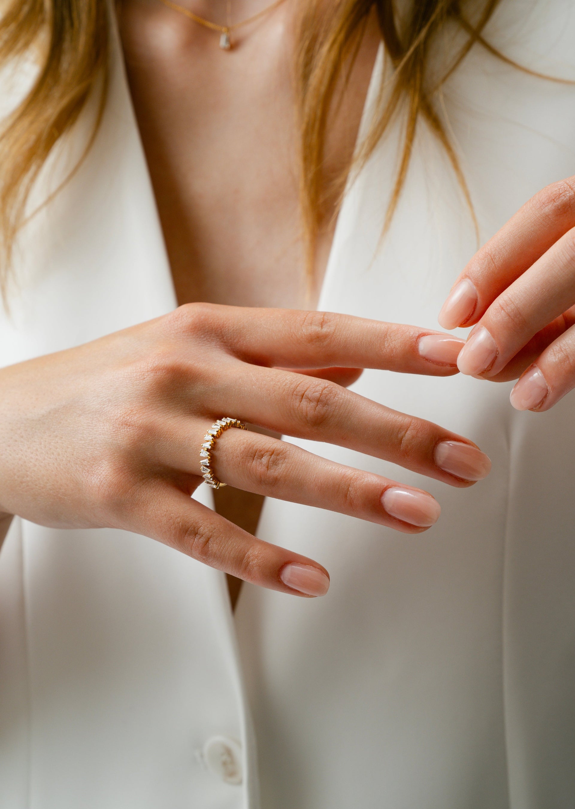 A close-up of a model wearing the Iggy Ring in gold, an eternity band design featuring sparkling tapered baguette-cut cubic zirconias, along with a fine gold chain necklace.