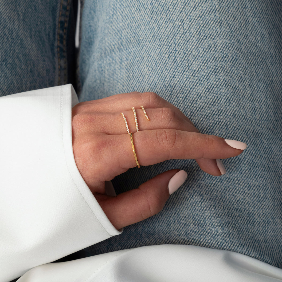 A close-up of a model wearing the Sparkle Wrap Ring in gold, featuring bands paved with cubic zirconia that wrap around the finger, paired with a simple thin gold band.