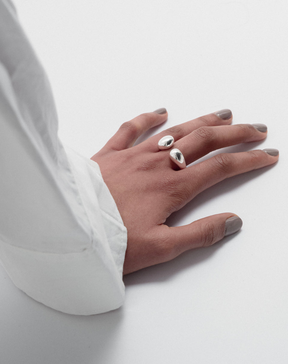 A shot of a model's hand wearing the Bolded Drops Ring in silver, highlighting its bold, open design with two drop-shaped ends.