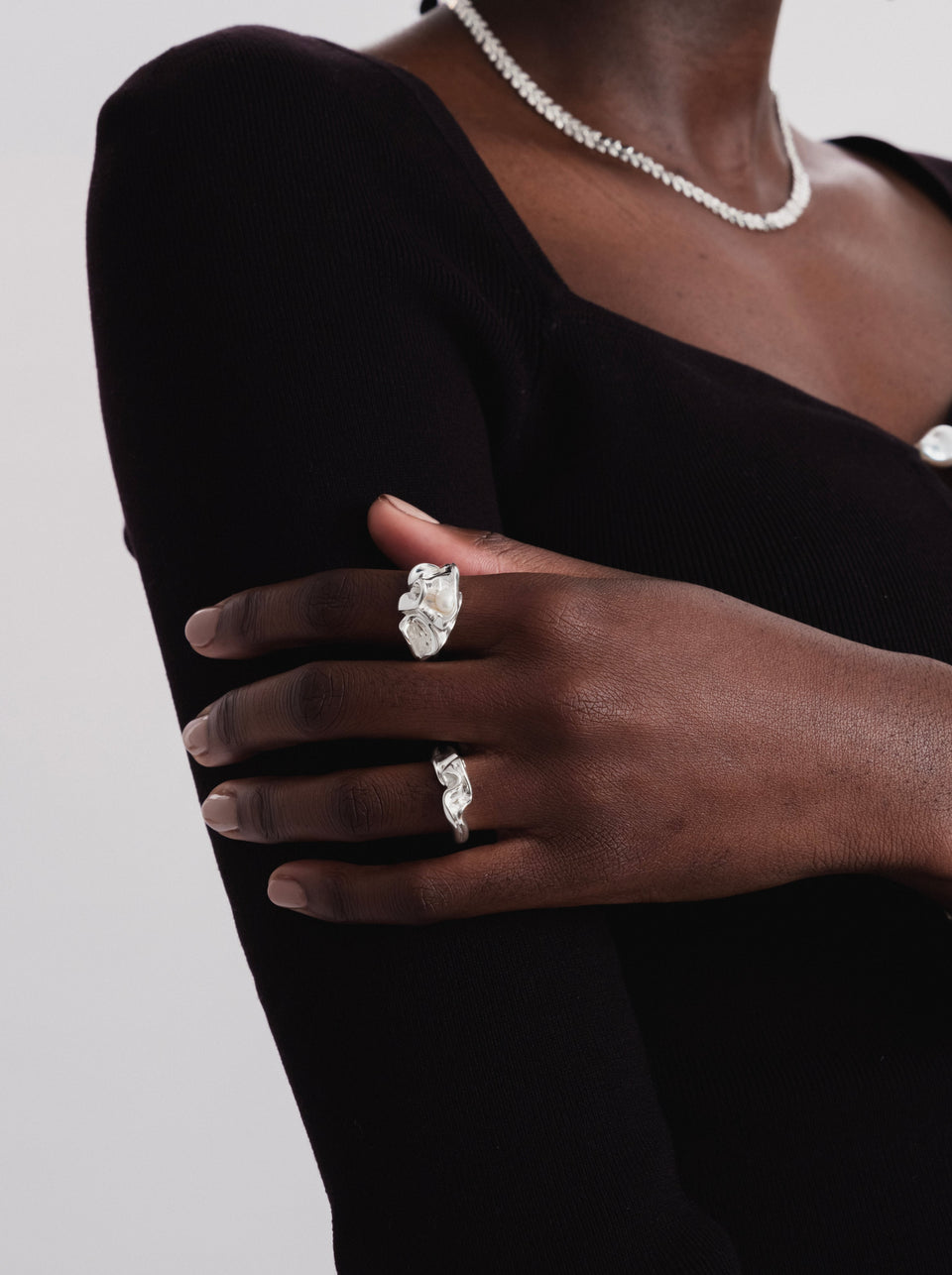 A model wears two rings from the Syster P Moulded collection, the Narrow Ring on her ring finger and a larger version on her index finger, paired with a matching textured silver necklace.