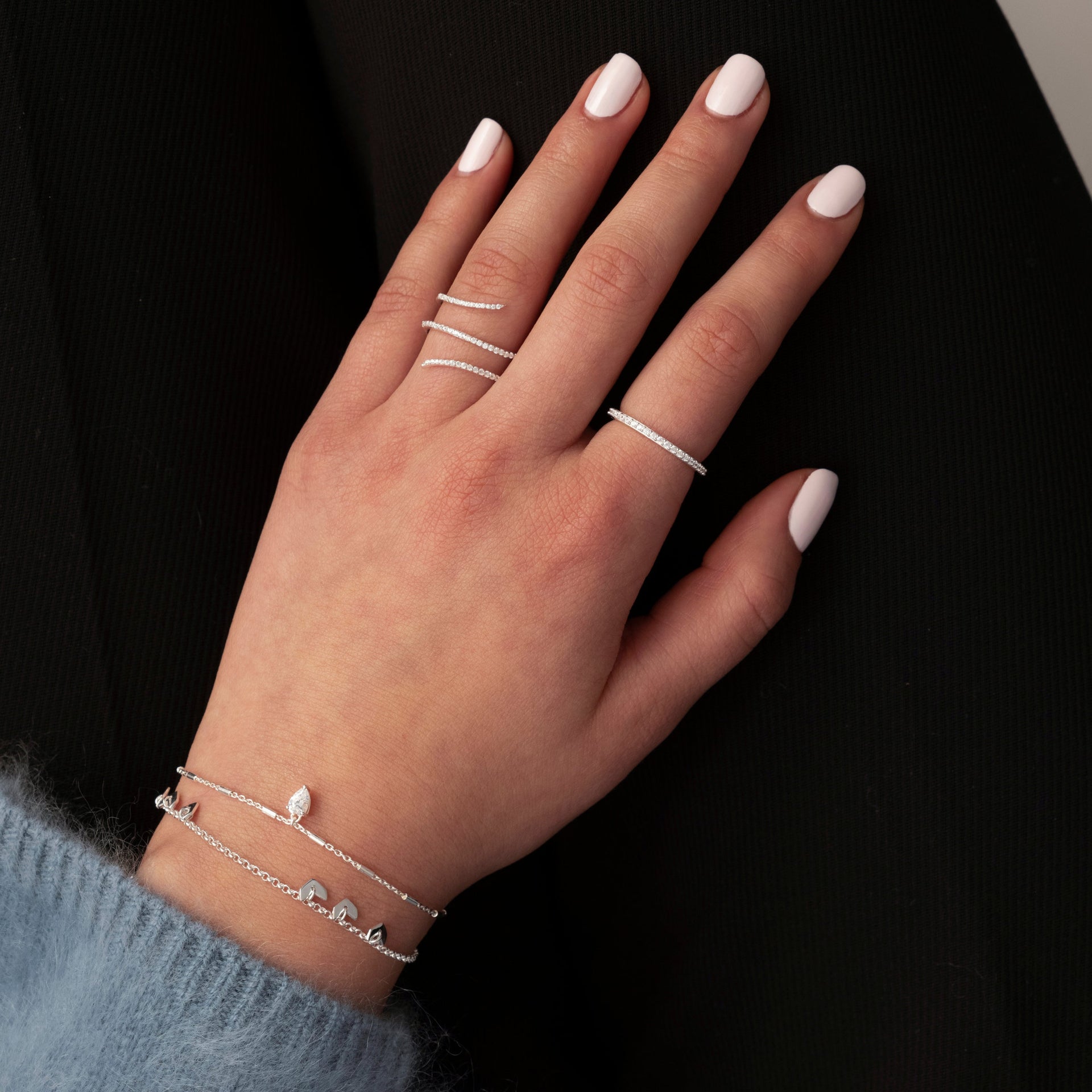 A close-up of a model wearing the Sparkle Wrap Ring in silver, which elegantly wraps around her middle finger, styled with another silver eternity ring and two delicate silver bracelets.