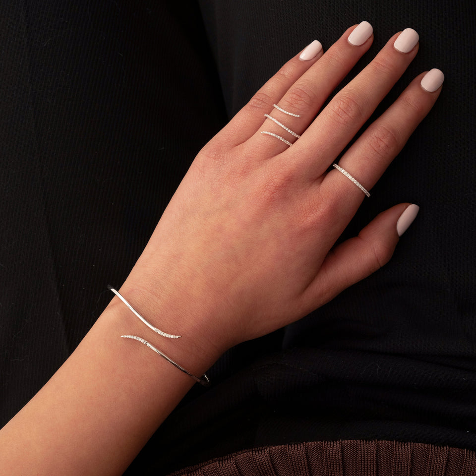 A model wears the Sparkle Wrap Bangle in silver, featuring curved ends set with cubic zirconia, paired with a matching silver wrap ring and a simple pav√© band ring.