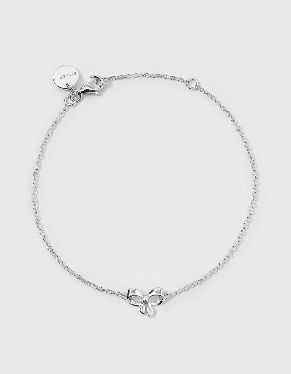A product shot of the Rosie Mini Bracelet in silver, laid out in a circle to display its design of a fine chain with a central bow-shaped pendant.