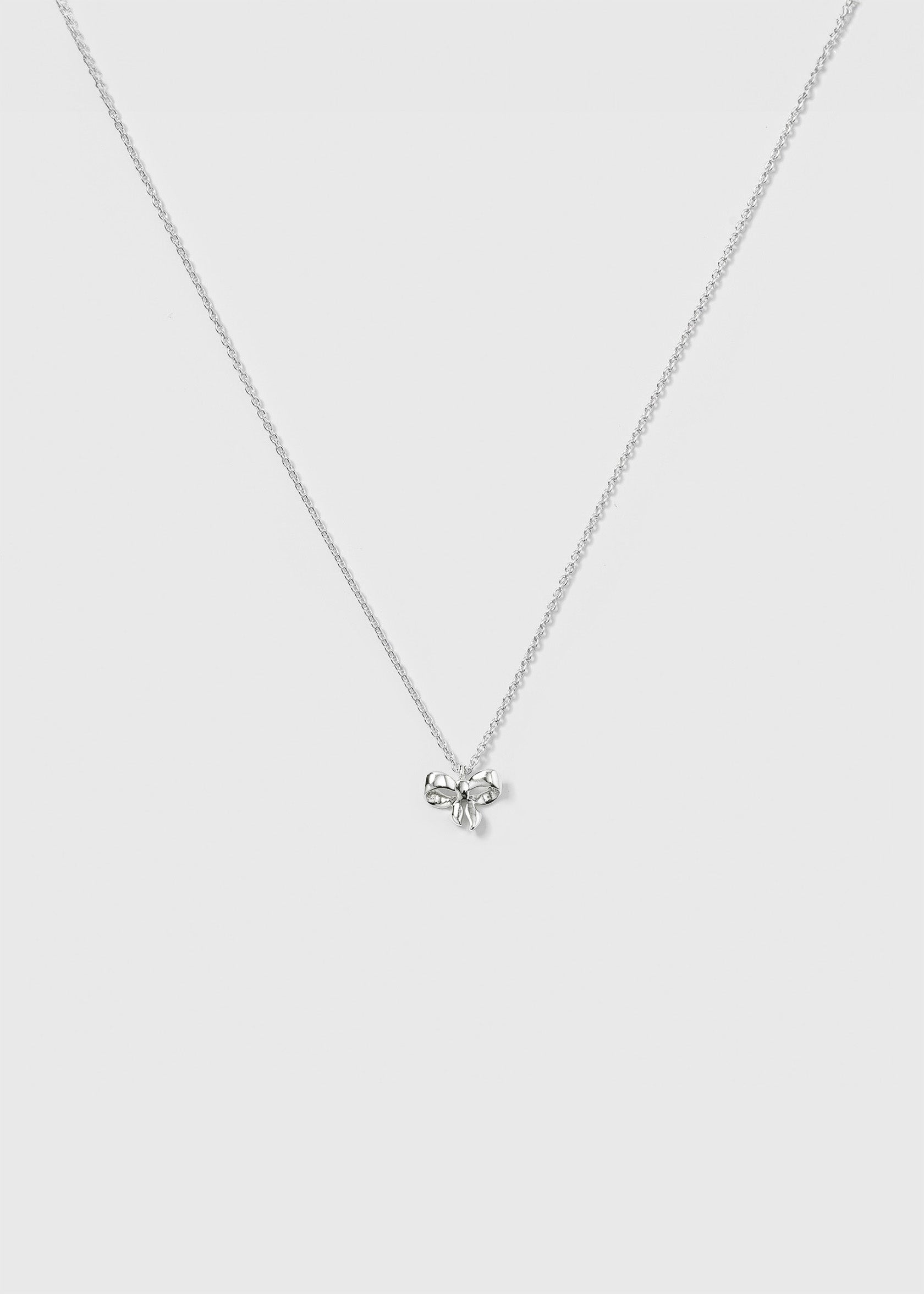 A product shot of the Rosie Mini Necklace in silver, featuring a delicate, sparkling chain and a small bow-shaped pendant.