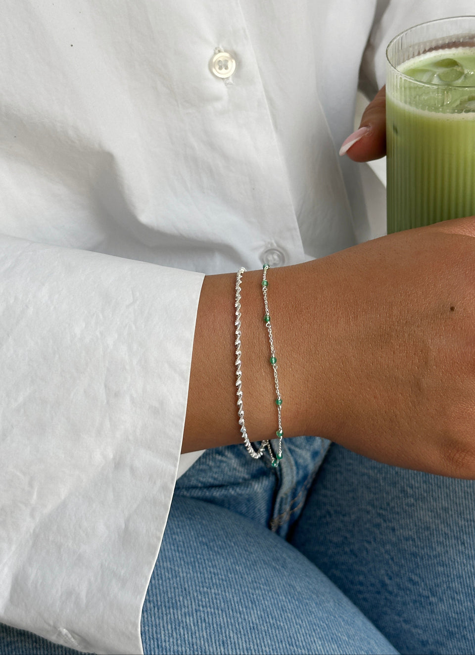 A model wearing two silver bracelets from Syster P on her wrist: the Santa Monica bracelet with green onyx beads, and a twisted silver chain bracelet.