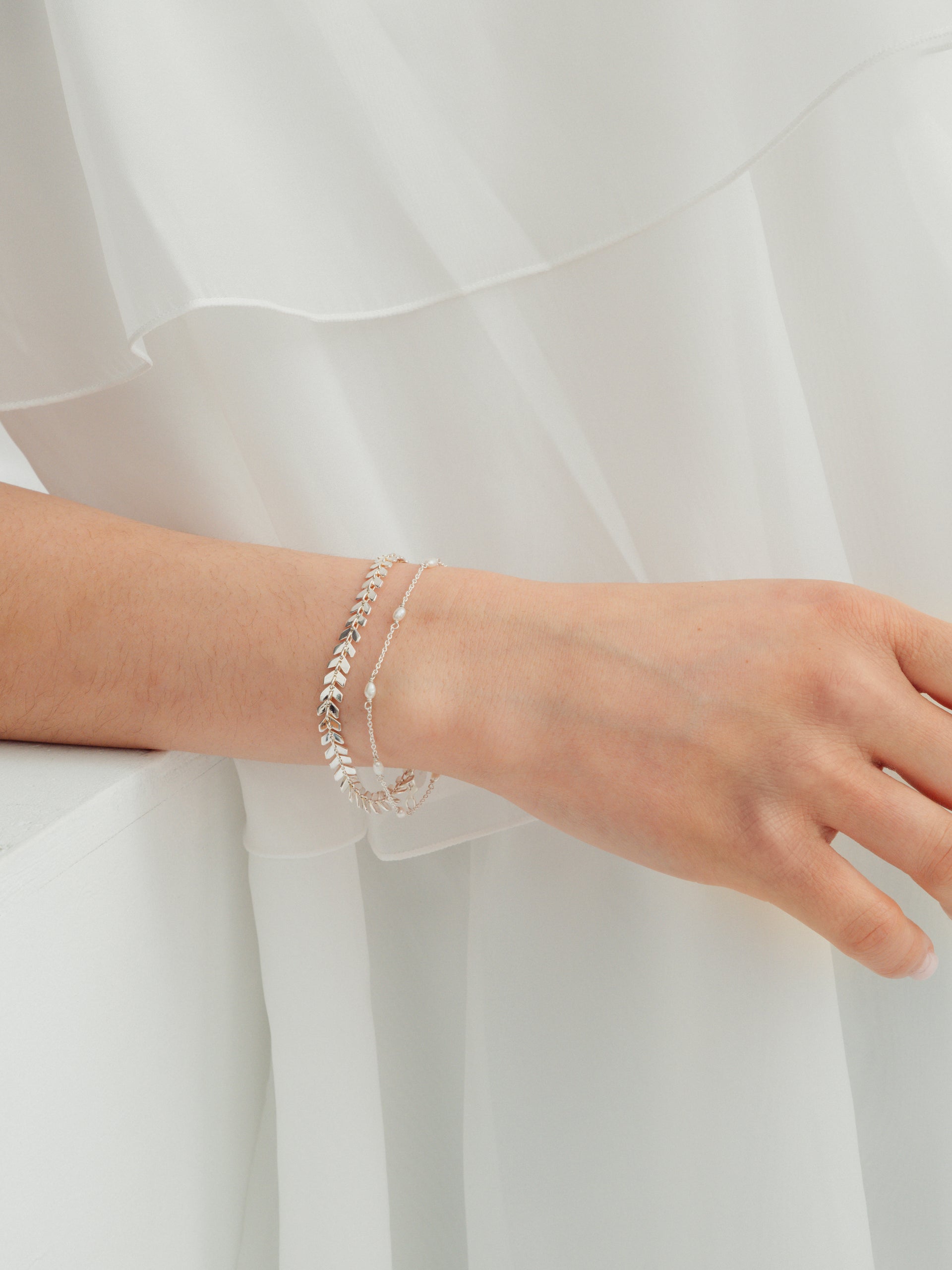 A model's wrist wearing the silver Layers Olivia Bracelet, featuring a leaf pattern, layered with the delicate Treasure Multi Pearl Bracelet.