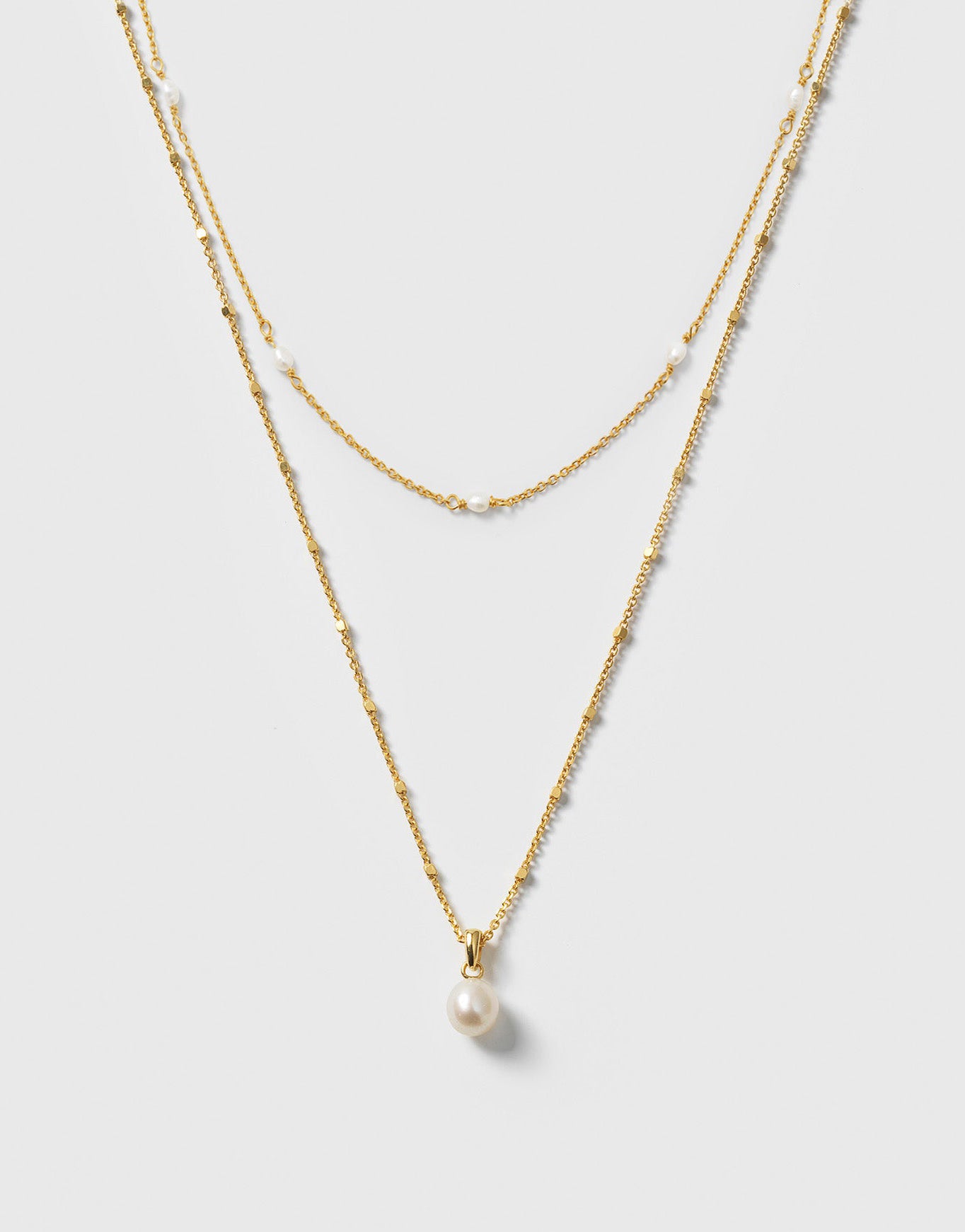 A product shot of the Treasure Necklace Set Gold, featuring two layered necklaces: a shorter one with multiple small freshwater pearls and a longer one with a single pearl pendant.