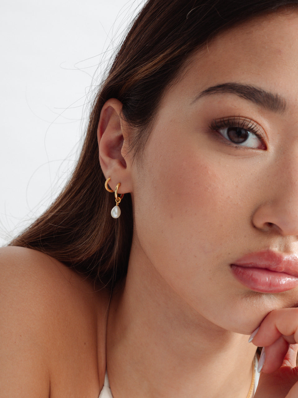A close-up shot of a model wearing the gold Beloved Twisted Small Hoops alongside the Treasure Pearl Hoops, which feature a dangling pearl.