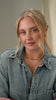 A model wearing a gold necklace with a leaf-like pattern, layered with a delicate gold chain with charms
