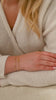A close-up of a model's wrist wearing the Bring Me Luck Bracelet in gold, featuring a delicate chain and a four-leaf clover charm, styled with Sheer Mirror Bracelet in gold, showcasing its delicate and smooth snake chain.