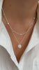 A close-up of a model wearing the Solea Necklace Silver, which has a delicate chain adorned with small hammered silver circles, layered with another silver necklace featuring a round hammered pendant.